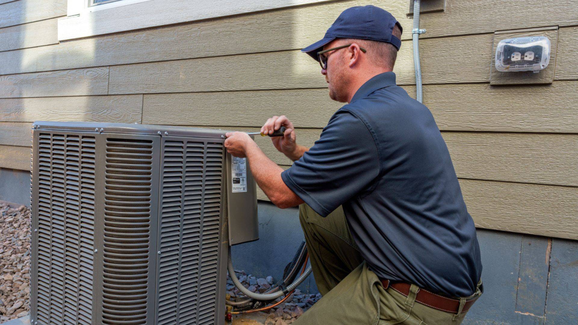 HVAC technician repairs an outdoor air conditioning unit next to a residential house in Colorado.