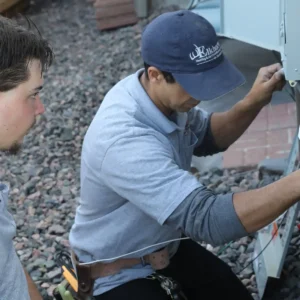 Two Elkhorn Heating Air Conditioning Plumbing and Electrical technicians servicing and repairing a residential backup generator electrical disconnect at a Denver Colorado home