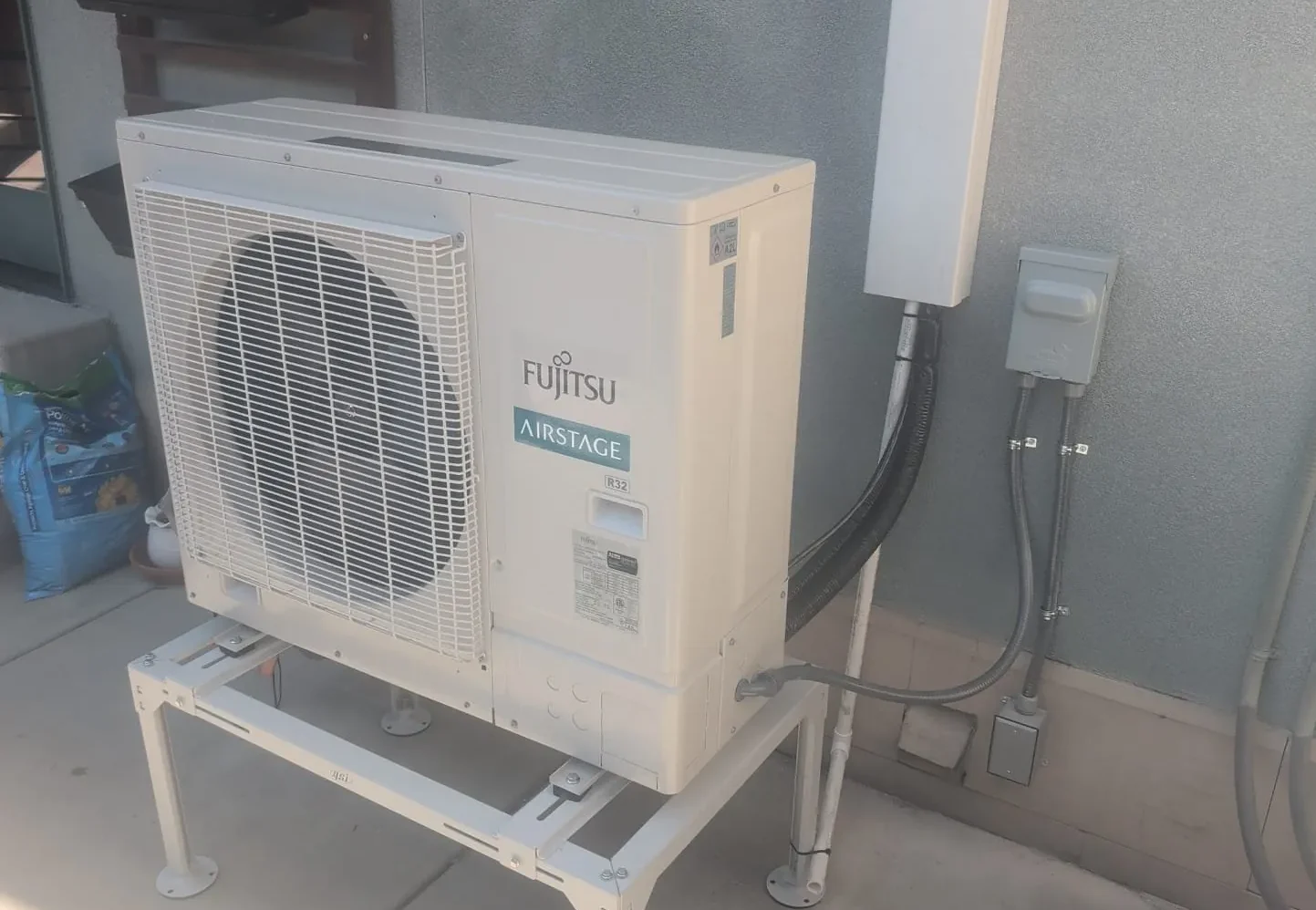 Fujitsu Airstage heat pump outdoor unit mounted on a raised stand beside a home