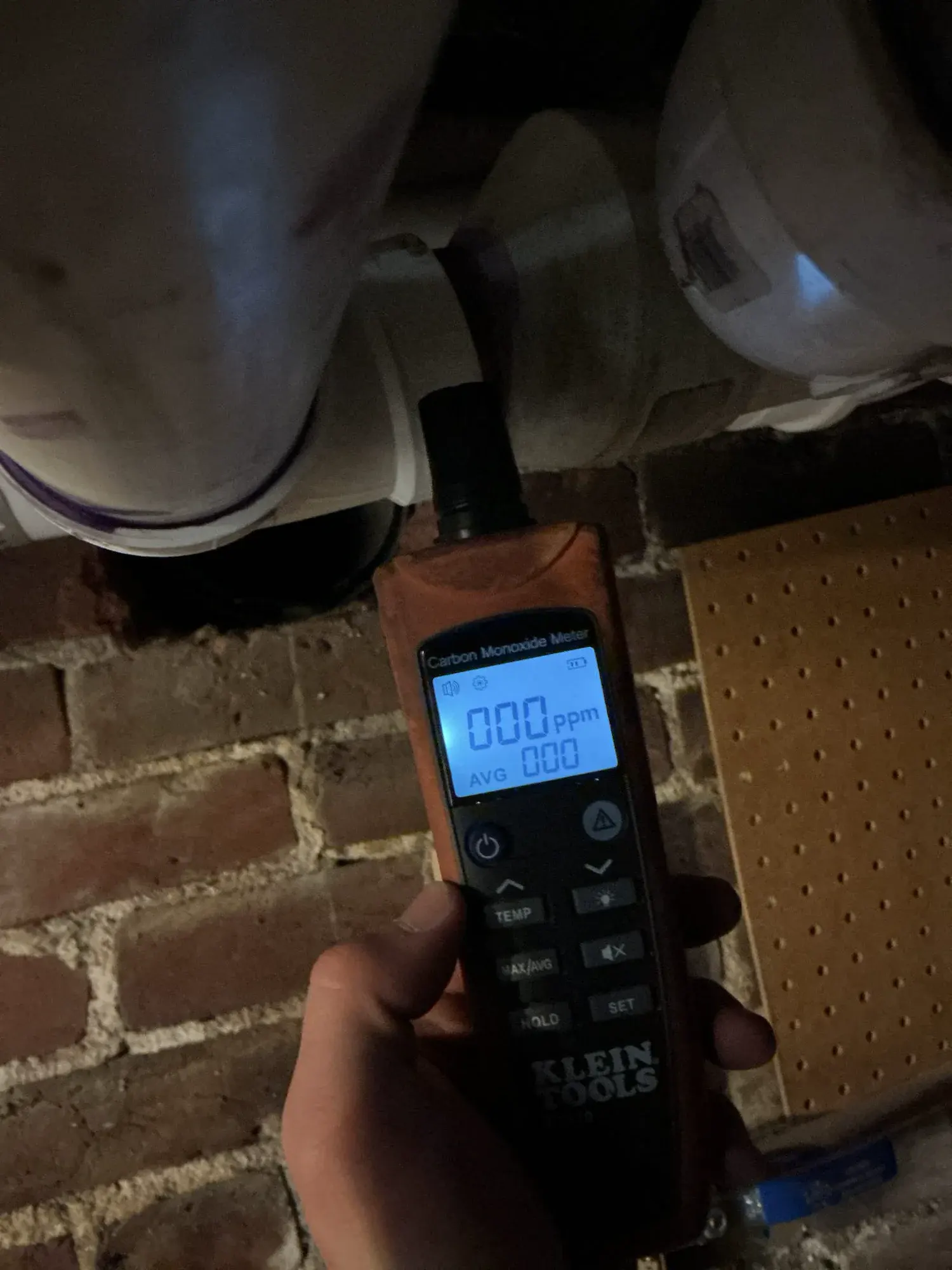 Handheld carbon monoxide meter beside white PVC flue piping during heating service in Denver.