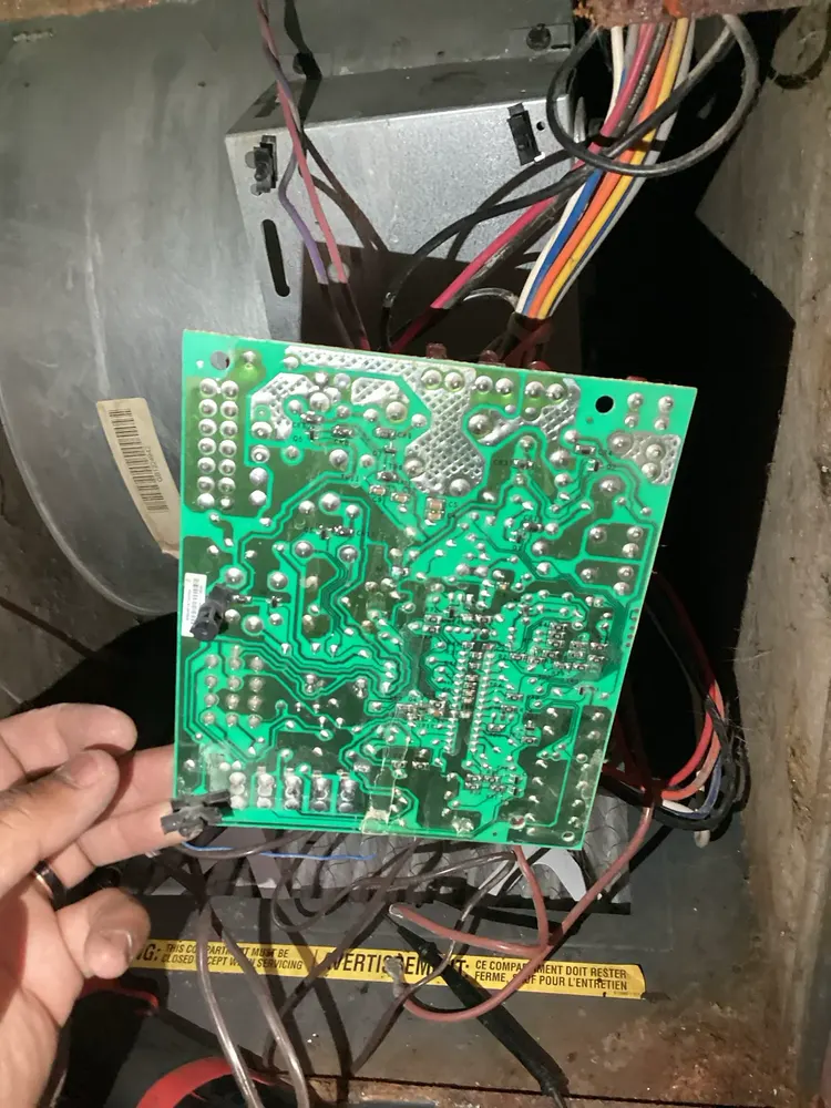 Control board held in front of an open furnace cabinet during a pilot-light diagnostic in Littleton.
